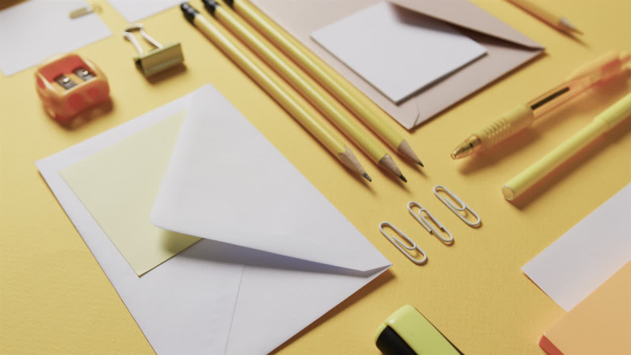 primer plano de bolígrafos, lápices y papelería dispuestos sobre un fondo amarillo, en cámara lenta