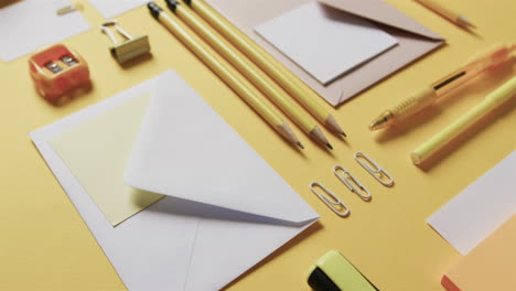 primer plano de bolígrafos, lápices y papelería dispuestos sobre un fondo amarillo, en cámara lenta