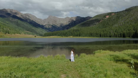 Aerial-cinematic-drone-following-female-women-model-actress-cute-dress-walking-toward-Piney-Lake-Ranch-Vail-Beaver-Creek-Colorado-Gore-Range-mountain-landscape-windy-breeze-summer-rain-sun-clouds-calm