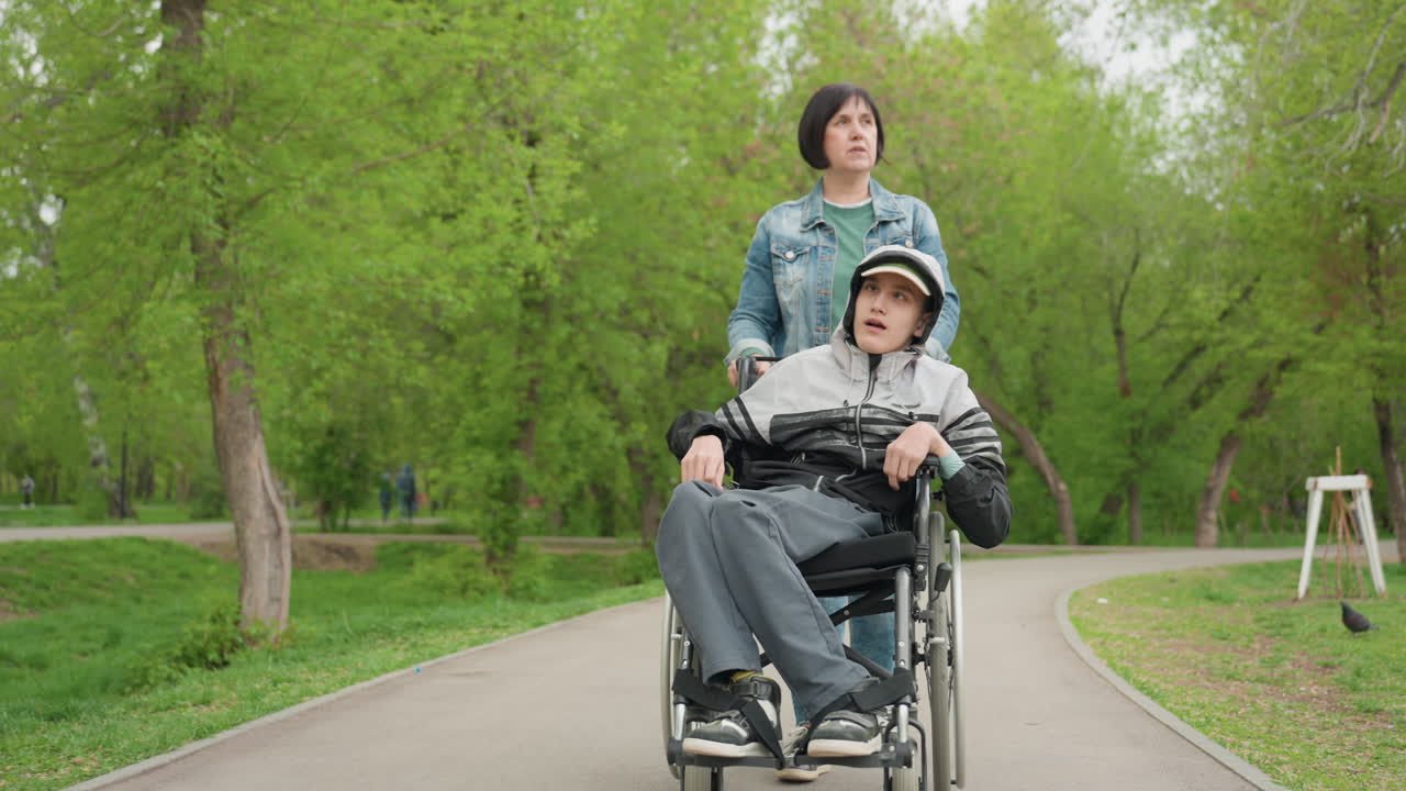Female Steadily Moves Wheelchair Through Park, Woman Gently Navigates Wheelchair Along Scenic Park Trail, Gentle Woman Assists Individual In Wheelchair Walking Through Lush Park Environment