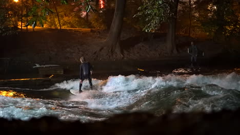 desvanecimiento cinematográfico cámara lenta eisbach onda río comunidad de surfistas de múnich alemania nivel del suelo ampliado en otoño otoño hermosa noche surf de alto flujo agua surf de los alpes de baviera superior flujo seguir el movimiento