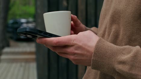 person holding smartphone and coffee cup outdoors