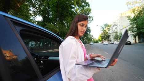 mujer joven trabajando en una computadora portátil al lado de un coche