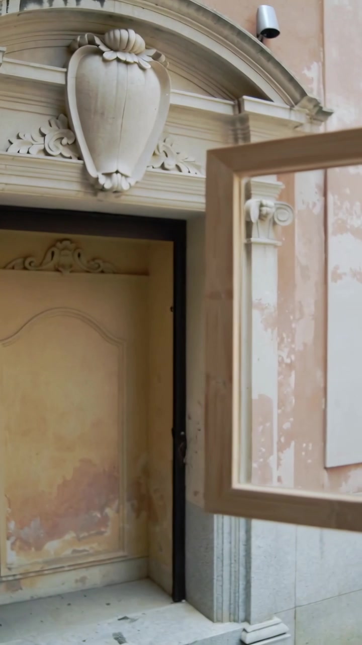 Video verticale: Sollevando una cornice di vetro con la mano destra, rivelando un arco intagliato sulla facciata, con spazio per il testo.
