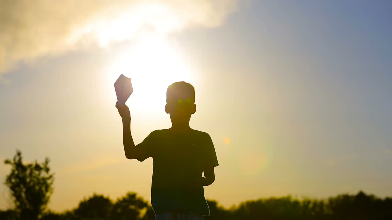 Child Playing With Airplane. Small boy playing with paper airplane at sunset near smoky pipes