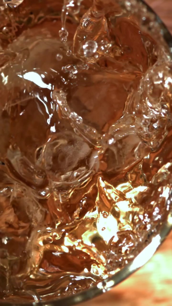 Versamento al rallentatore di una bevanda ambrata rinfrescante su ghiaccio
