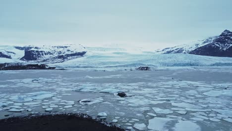 Snowy-mountains-near-glacier-in-volcanic-terrain-against-overcast-sky