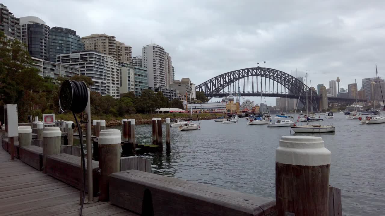 Northern shore waterfront with view of Harbour Bridge, buildings and boats on the water on an overcast day, Stabilized walking pan right shot