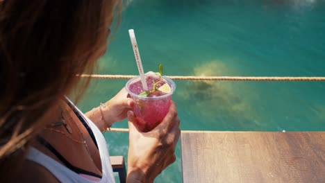 woman drinking refreshing beverage, sitting near lake in sunny, windy, summer weather