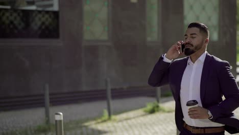 businessman holding paper cup and talking by cell phone outdoor