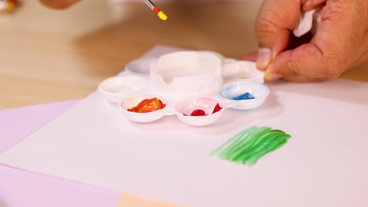 Close-up of hand mixing watercolor paints on palette, bright lighting, shallow depth of field