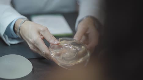 doctor showing patient breast prosthesis, plastic surgeon manipulating silicone and poking with finger close-up