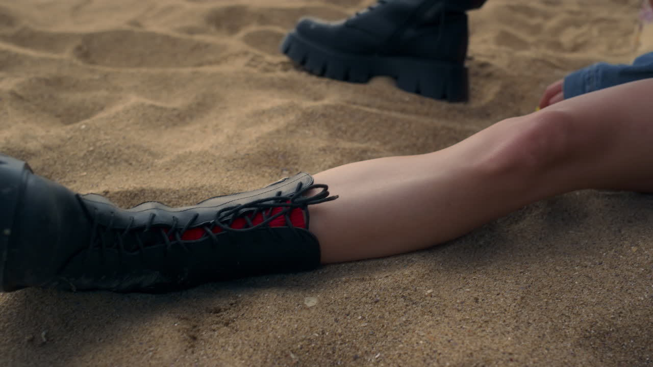 검은 부츠를 입은 노란색 해변 모래에 누워있는  ⁇ 은 다리의 매력적인 소녀.