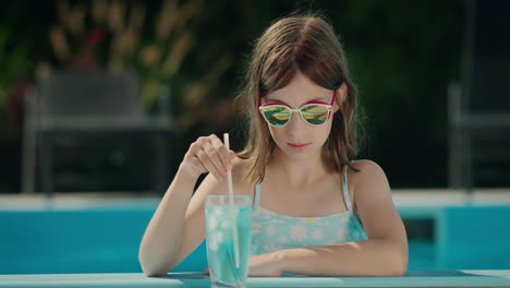 teenage girl crushes ice in a cocktail on the side of the pool