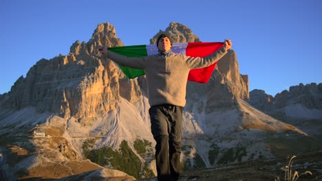 imágenes filmadas en rifugio auronzo, tri cine en las montañas de los dolomitas italianos con un hombre moviéndose y sosteniendo una bandera italiana y con hermosas montañas en el fondo, filmadas al amanecer en 4k