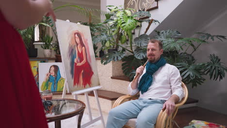 woman model brings cup of tea to artist. professional painter evaluates live model with gaze sitting with paint brush in hand taking break from drawing