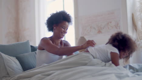 african american mother tickling her little daughter and having fun together in the bed