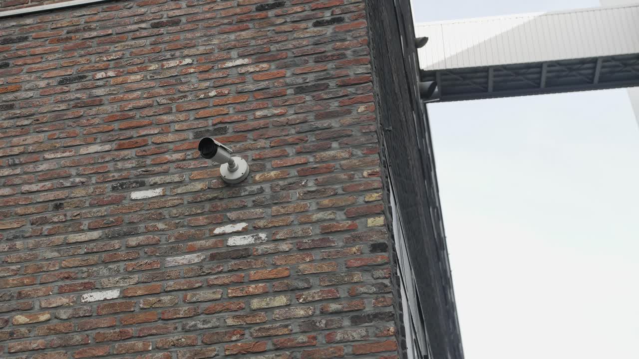 Security camera affixed to a textured brick wall, overseeing an industrial area
