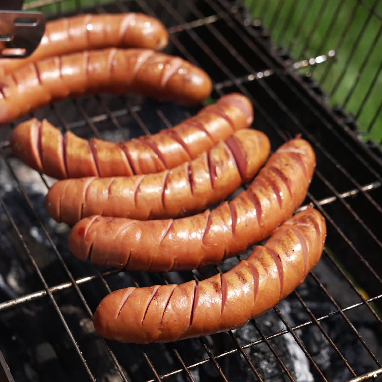 Tasty juicy sausages grilling. Barbecue grill cooking outdoors. Hot dog sausages are turning with tongs on a grill plate. Food for picnic