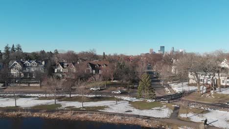 aerial footage following a car at lake of the isles,nice neighborhood during a sunny afternoon and showing downtown minneapolis in the background