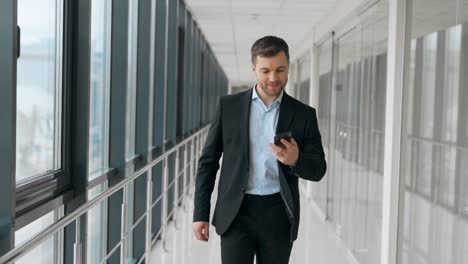 business adult man walking down the hall receives a joyful message on a smartphone