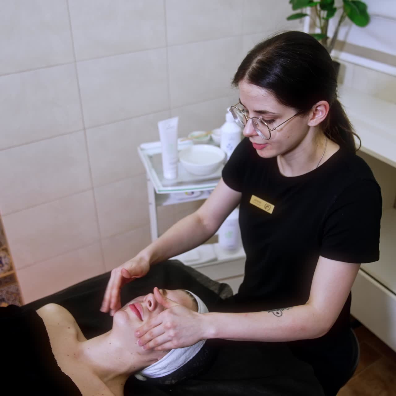 Cosmetologist performs facial massage to a client. Specialist performs round movements on the female face. Top view