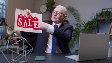 man in suit points to a sale sign