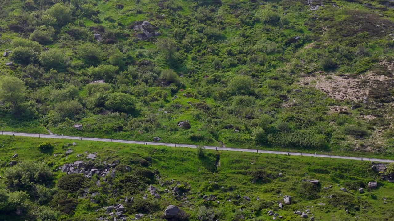 Close-up drone view of rugged alpine hillside with retaining walls and a high-altitude road barely visible