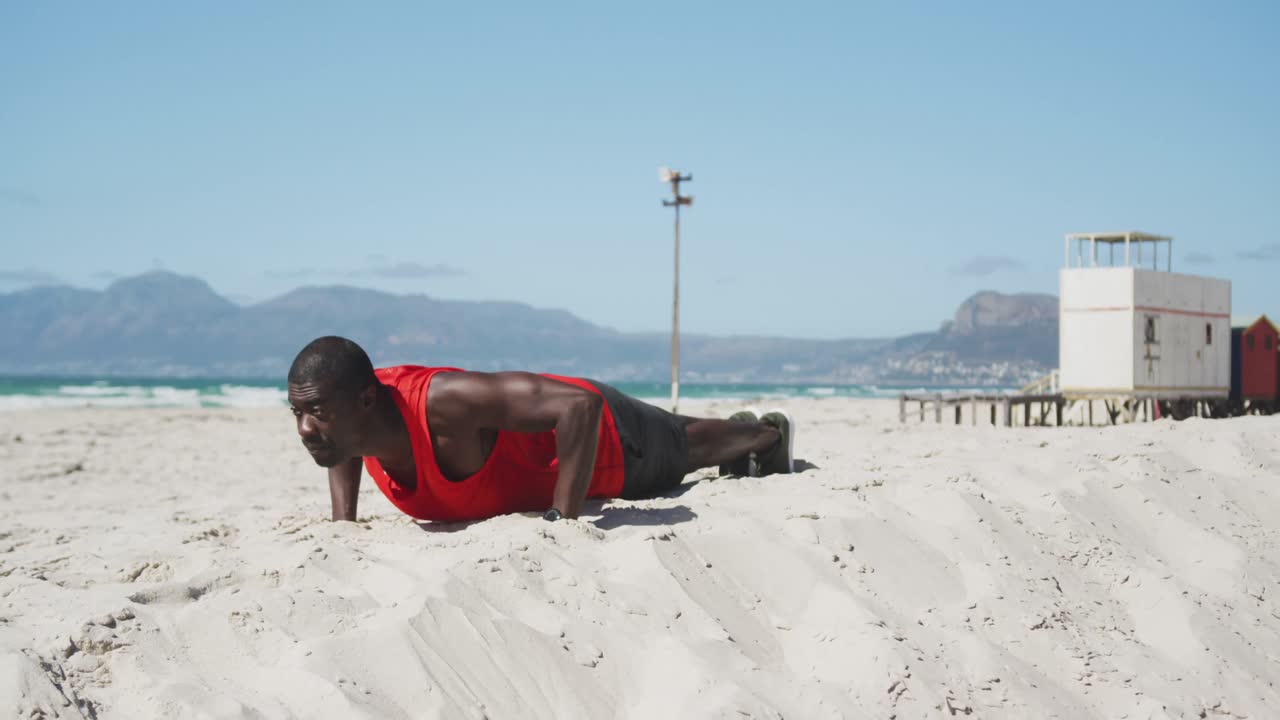 Focused african american man doing press ups on the beach, exercising outdoors by the sea