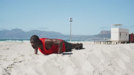 Focused-african-american-man-doing-press-ups-on-the-beach,-exercising-outdoors-by-the-sea