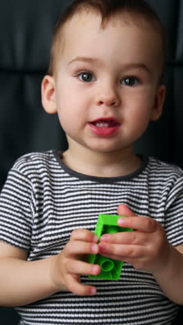 beautiful caucasian kid sits in a black office chair. cute child turns a piece of constructor and says something. vertical video