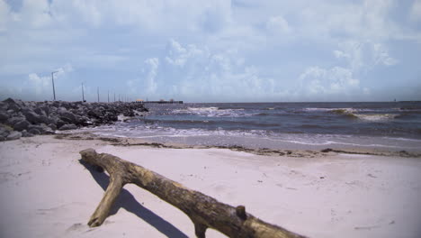 shallow wave crash upon the shore of a white sand beach as a lonely driftwood branch lies in the foreground on a white sand beach on a sunny day in gulfport, mississippi