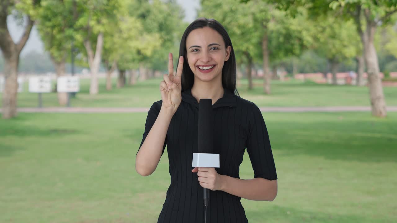 Happy Indian female news reporter showing victory sign