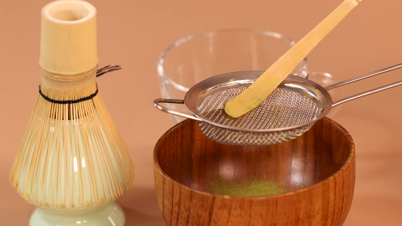 Primo piano di tè matcha in polvere setacciato attraverso un colino di metallo in una ciotola di legno