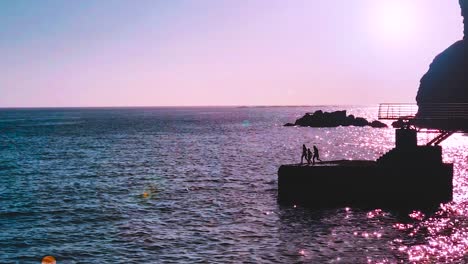 three children run and jump together into sea from pier at sunset