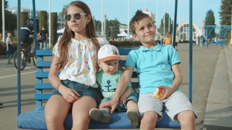 relaxed little kids sitting on swing. cute three siblings spending time outdoors