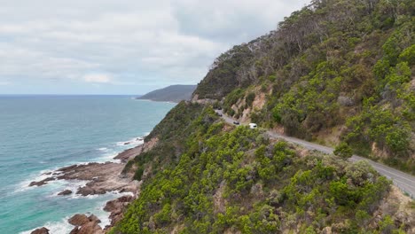 aerial view of a car driving along the coastal great ocean road in lorne, australia, surrounded by lush greenery and ocean views