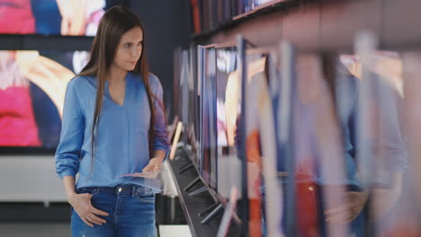 una mujer inteligente y moderna elige grandes televisores en una tienda de electrónica. nuevas generaciones de pantallas.