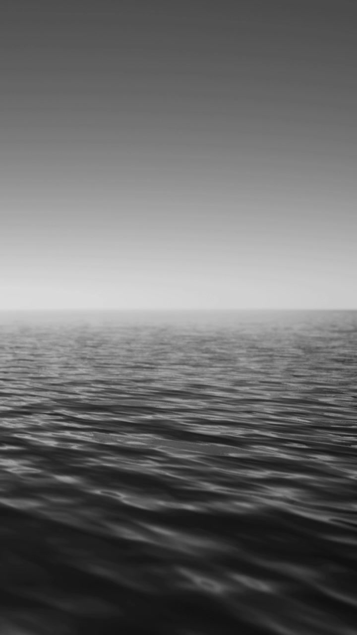 Waves move softly across a calm sea under a clear sky at dawn