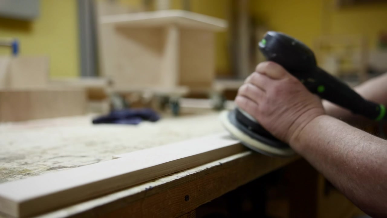 Hands Orbital Sander On Plywood Edge, Closeup Action With Rotary Pad Removing Roughness, Workbench Background. Media