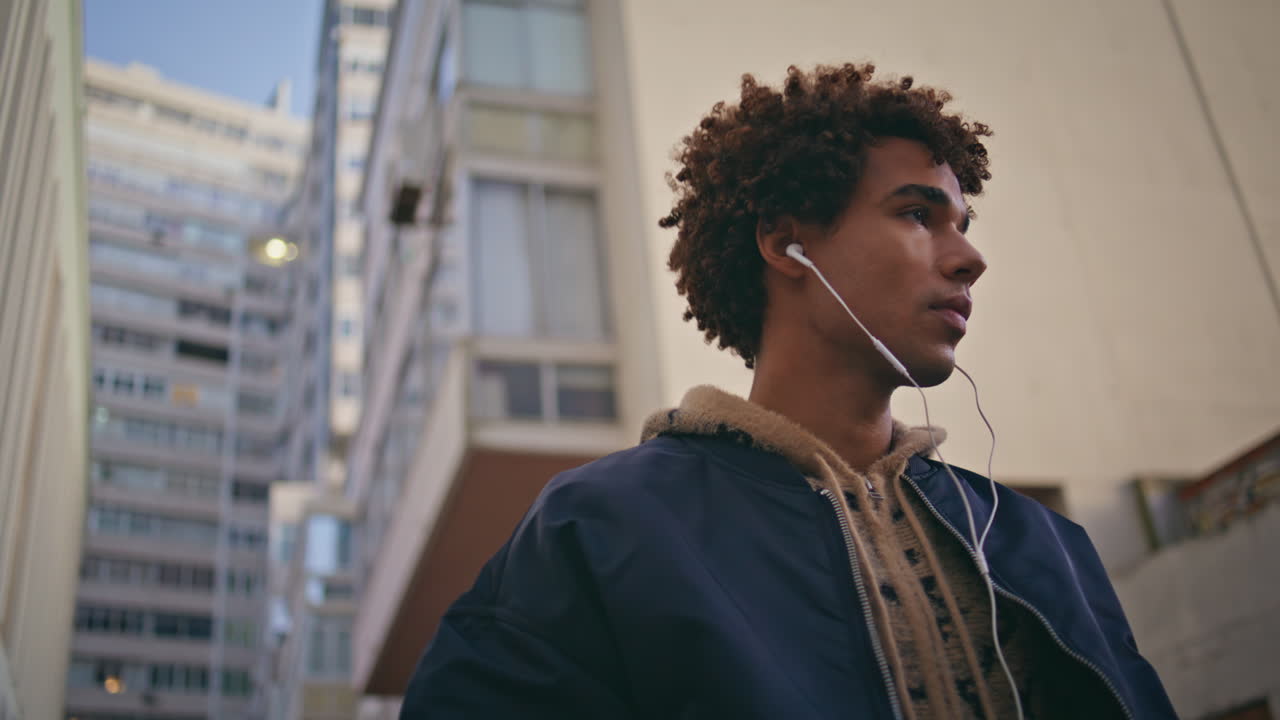 Young melomaniac listening music in headset walking near urban buildings closeup