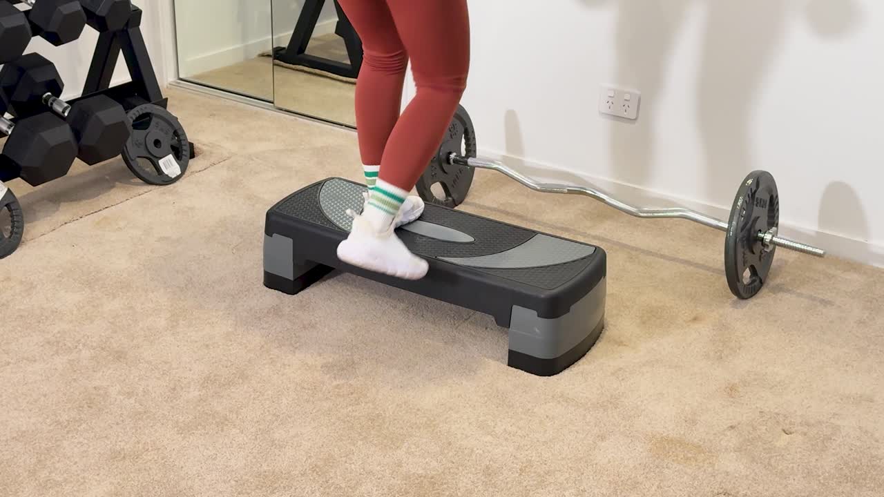 A woman performs step exercises with dumbbells in a home gym setting, focusing on fitness and strength