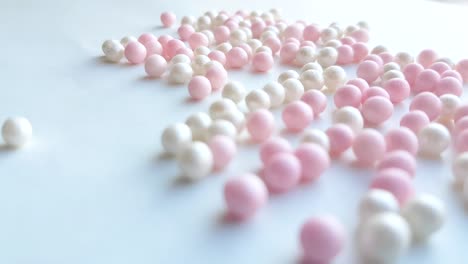 pequeñas bolas blancas y rosas de madreperla o cuentas de polvo de maquillaje rodan sobre un fondo blanco, concepto de idea minimalista, video 4k