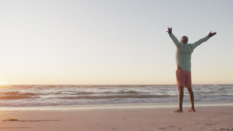 un anciano afroamericano feliz abriendo los brazos en la playa, en cámara lenta, con espacio para copiar