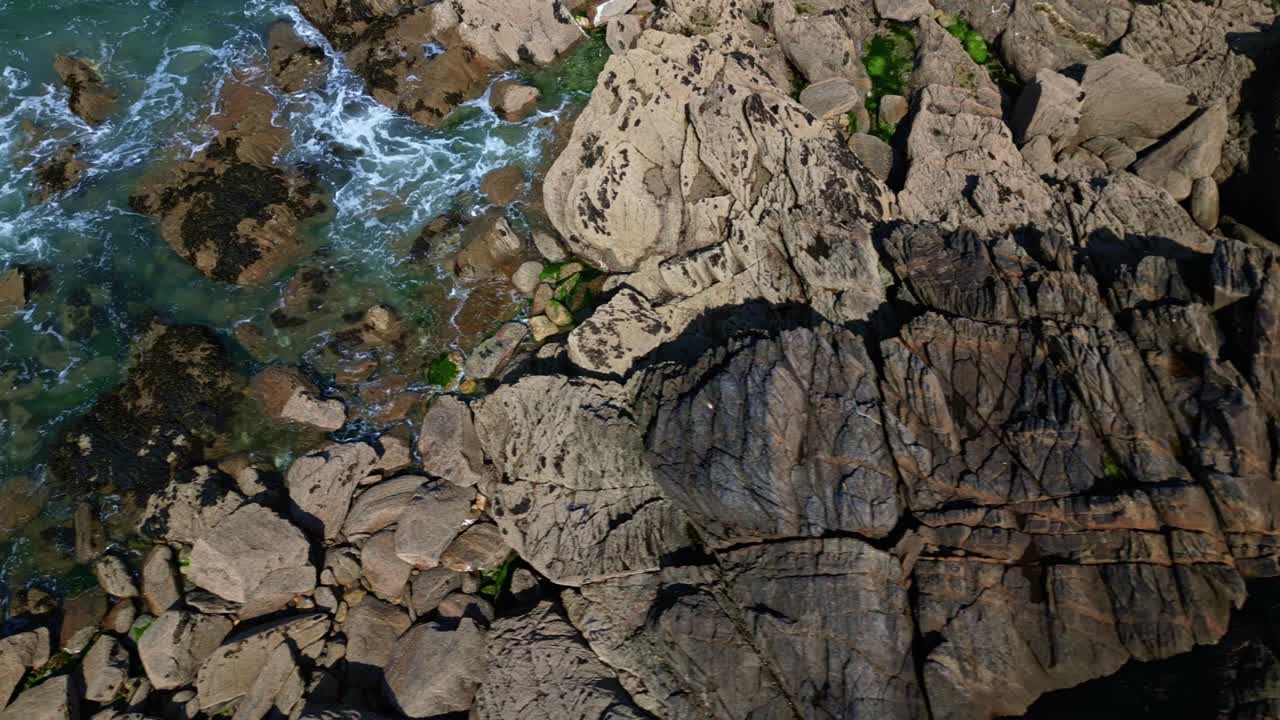 Overhead drone shot of rugged rocks in Brittany as waves crash against the shoreline - France