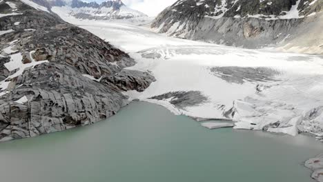 aerial flyover over the glacial lake of rhone glacier at furkapass, switzerland at the beginning of summer with big ice chunks and icebergs in the water