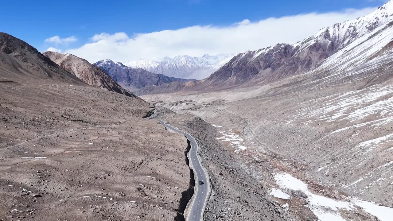Aerial drone shot capturing a car winding through a narrow valley, with towering cliffs on either side in Ladakh.