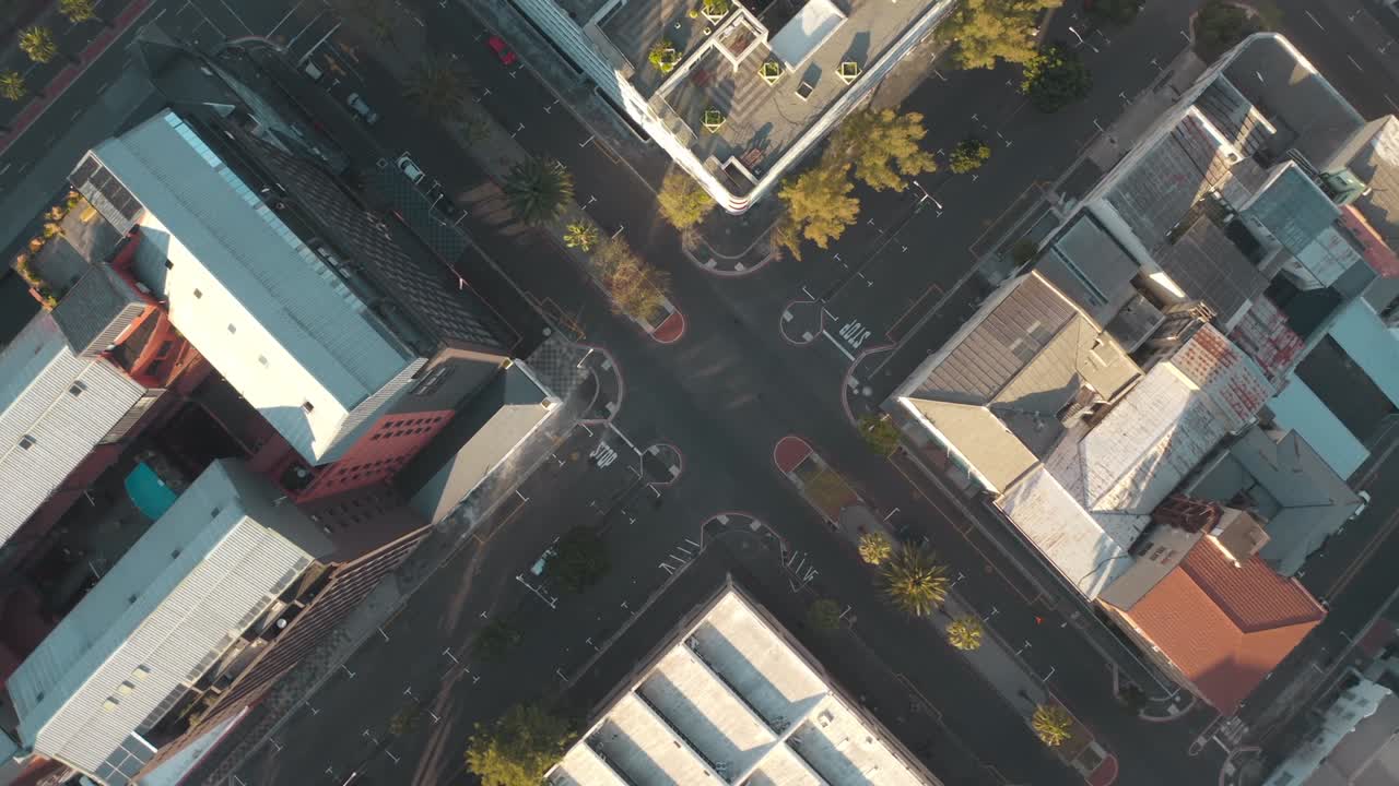 Overhead drone view reveals city's intricate network of buildings and roads on sunny day, with clear sunlight highlighting organized streets, bustling intersections