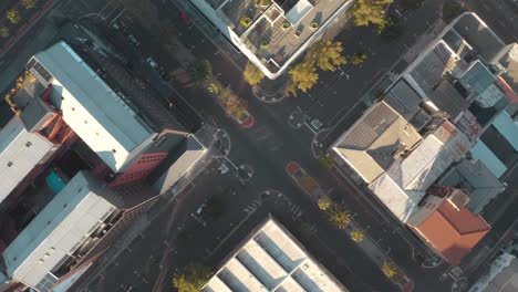 overhead drone view reveals city's intricate network of buildings and roads on sunny day, with clear sunlight highlighting organized streets, bustling intersections