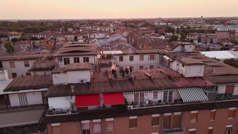 Drone-shot-of-a-group-of-people-dressed-in-black-lighting-some-red-smoke-bombs-on-a-rooftop-at-sunrise